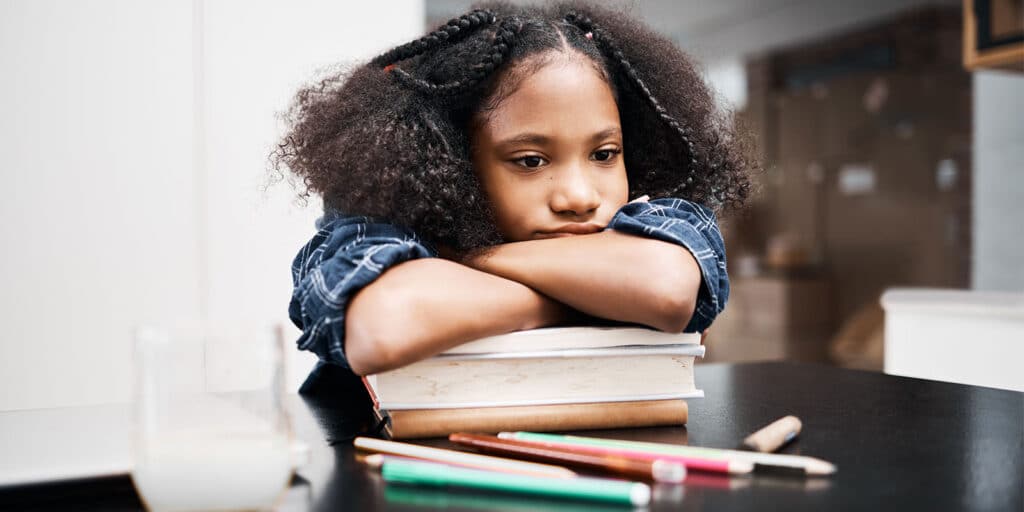 A young girl sitting at the table with her head on top of books.