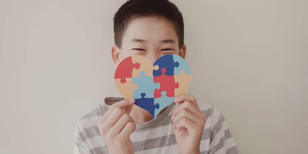 A boy holding up a puzzle heart shaped piece of paper.