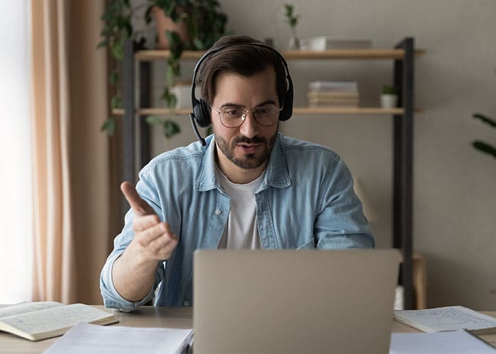 A man wearing headphones and sitting at a table with a laptop.