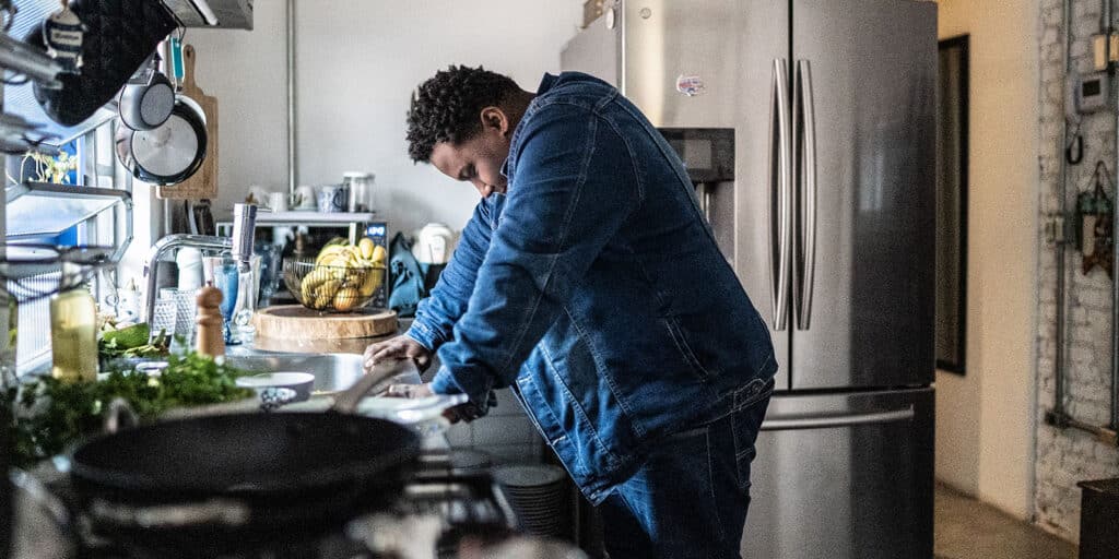 A man in blue jacket standing at counter preparing food.