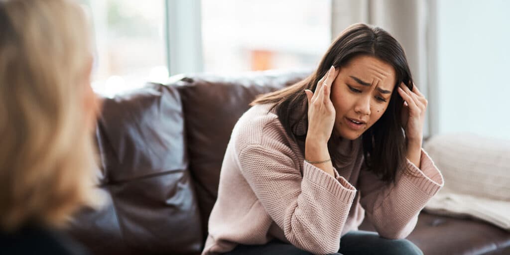 A woman sitting on the couch with her hand to her ear.