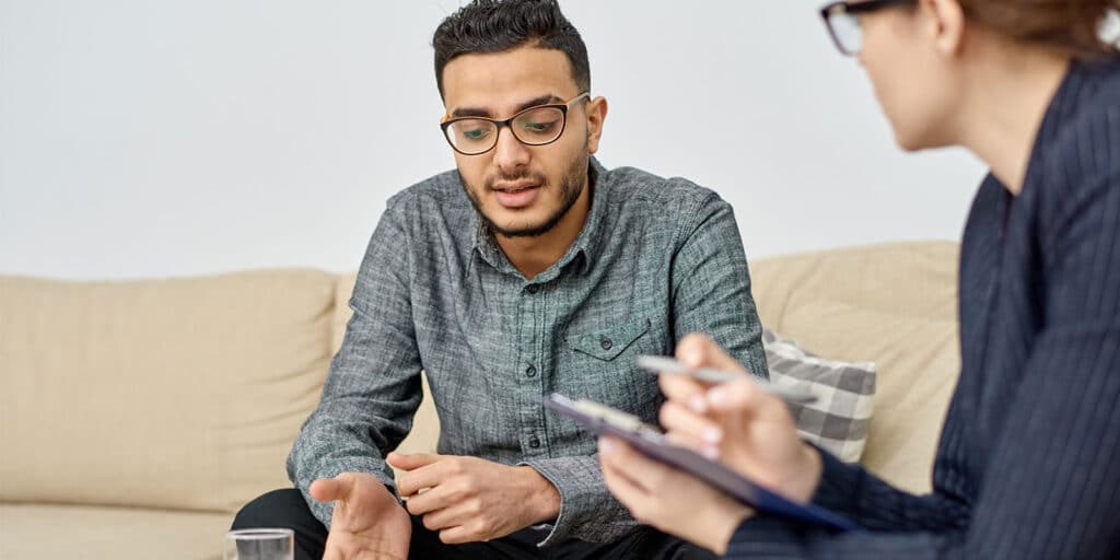 A man sitting on the couch talking to another person.