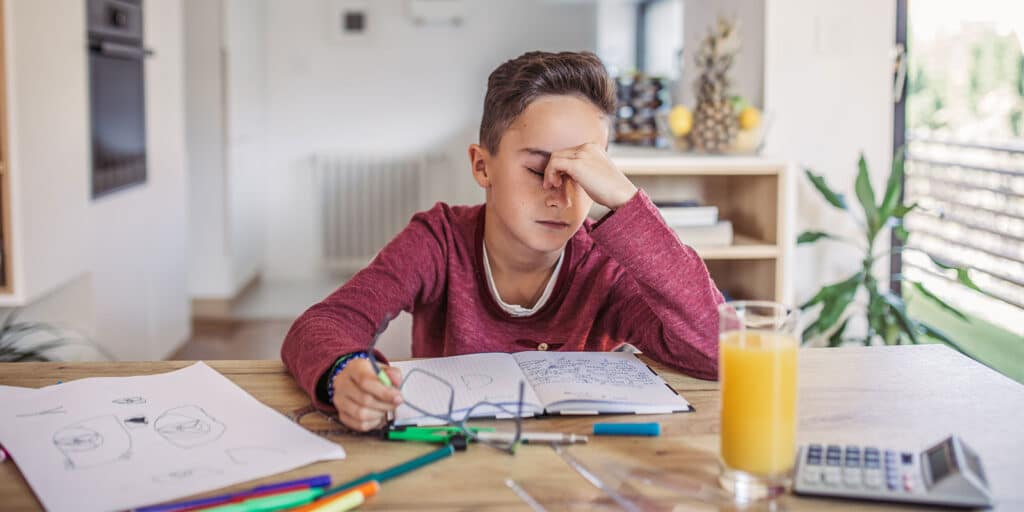 A boy sitting at the table with his hand on his face.