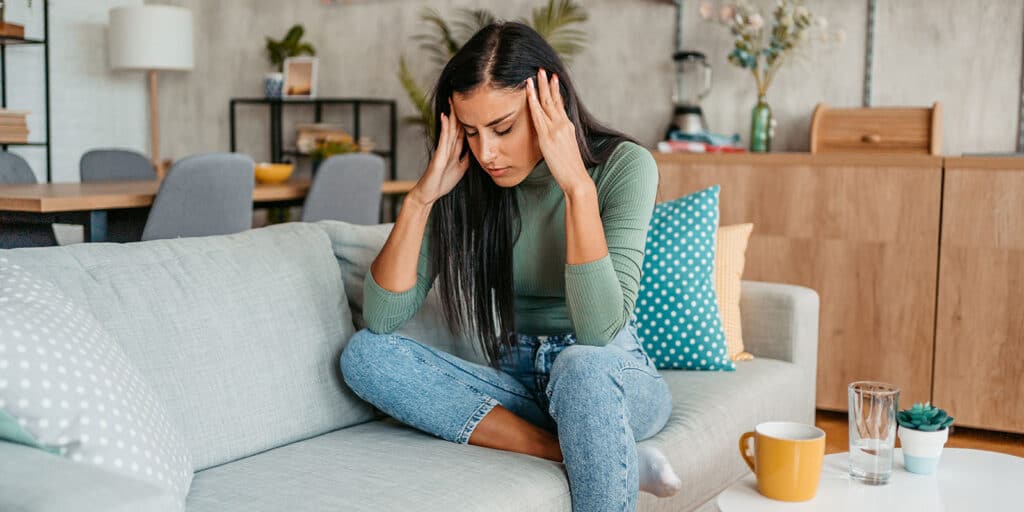 A woman sitting on the couch with her hands in her head.