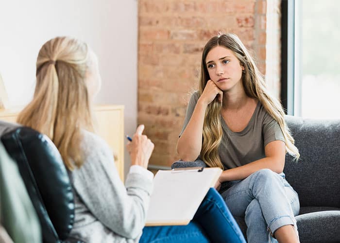 Two women sitting on a couch talking to each other.