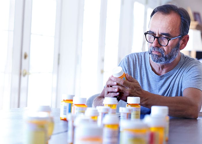 A man sitting at the table with many bottles of pills.