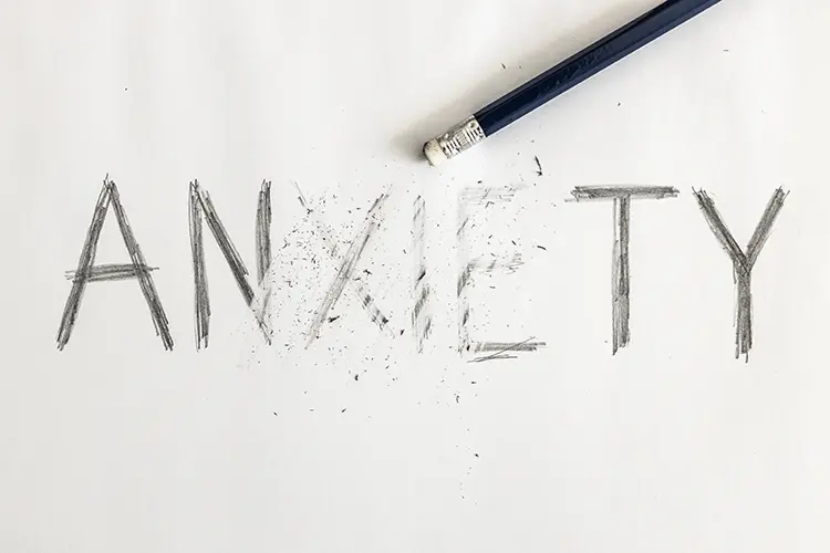 the word anxiety written on a piece of paper with a pencil erasing a part of the word